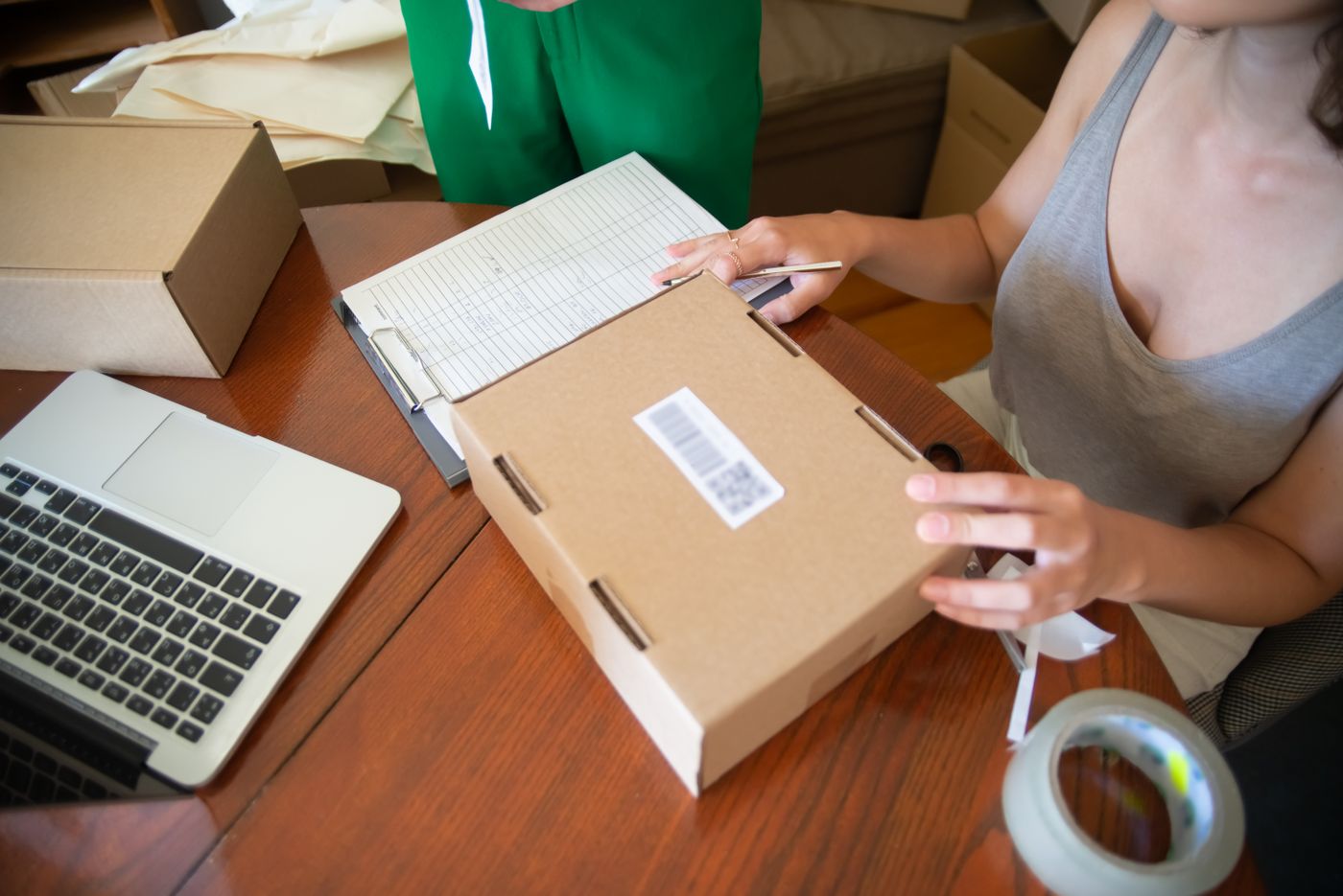 A person checking an order list beside a laptop and packed parcels.